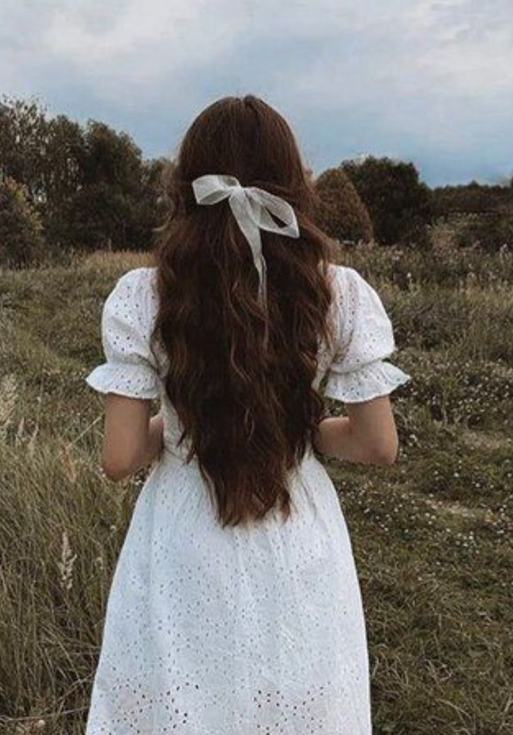 a woman standing in a field with her back to the camera, wearing a white dress