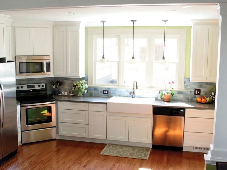 a kitchen with stainless steel appliances and white cabinetry, hardwood flooring, and large windows