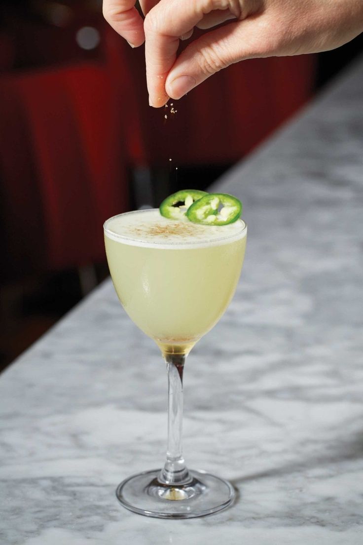 a hand is sprinkling a slice of cucumber into a cocktail