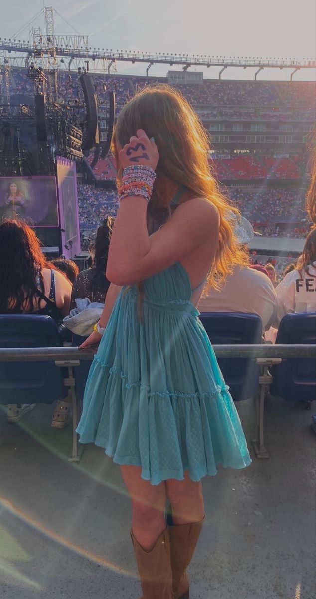 a woman standing in front of a stadium holding a cell phone to her ear and wearing cowboy boots