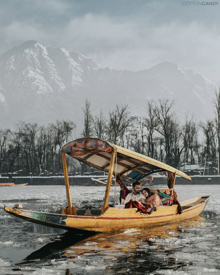 two people in a small boat on the water with mountains in the backgroud