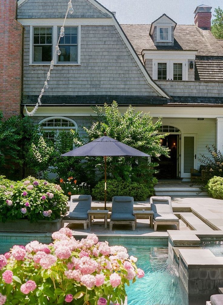 a house with a pool and patio furniture in the front yard, surrounded by flowers