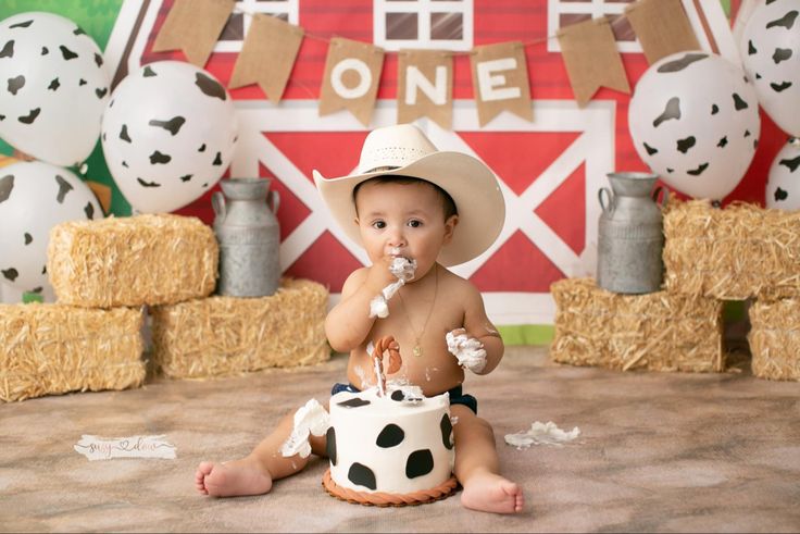 a baby sitting on the floor with a cake in front of him wearing a cowboy hat