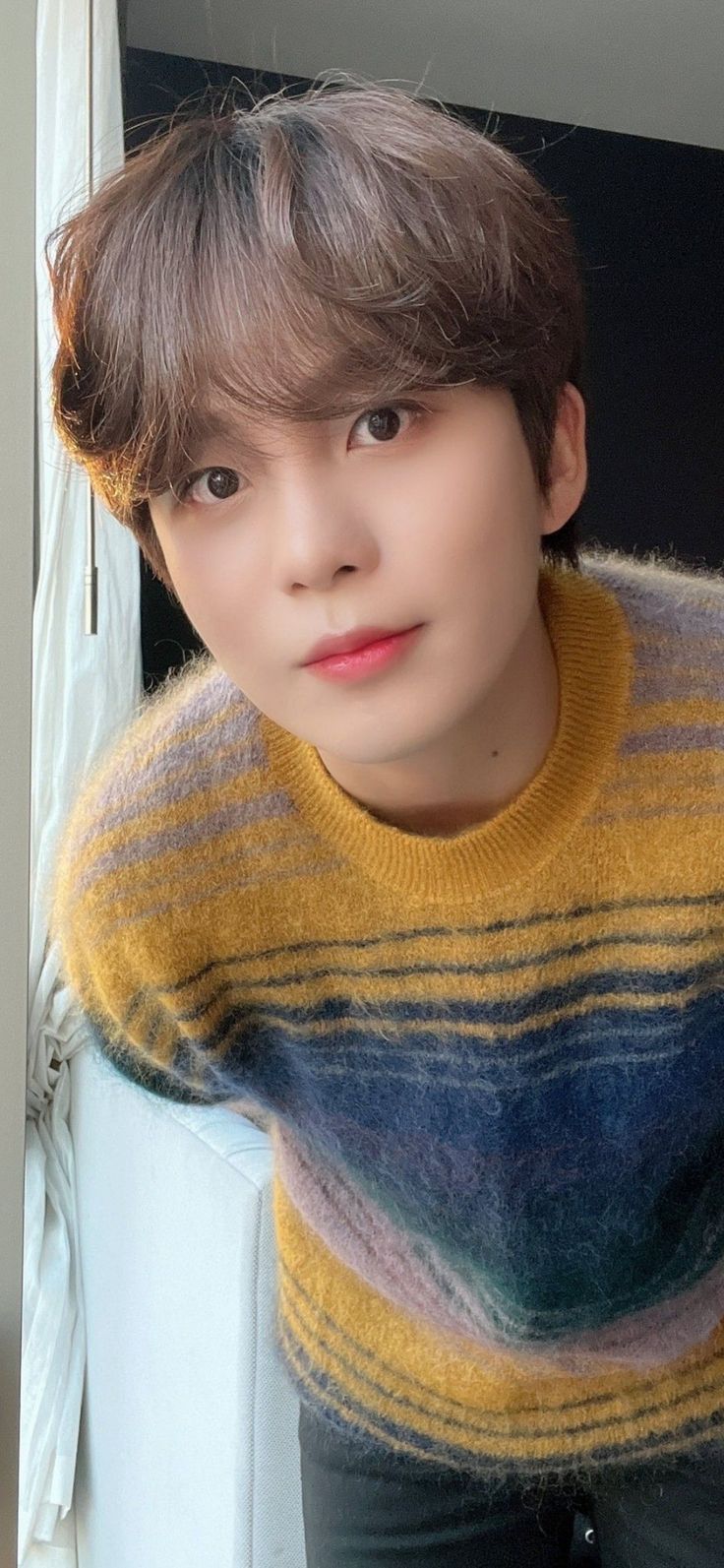 a young man with brown hair wearing a yellow and blue striped sweater