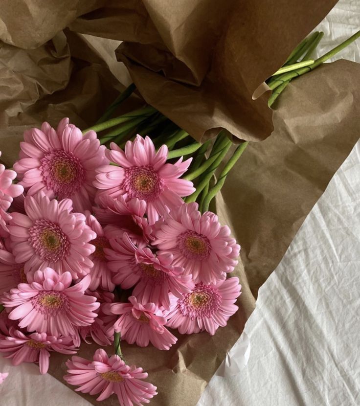 a bunch of pink flowers sitting on top of a white sheet covered table next to brown paper