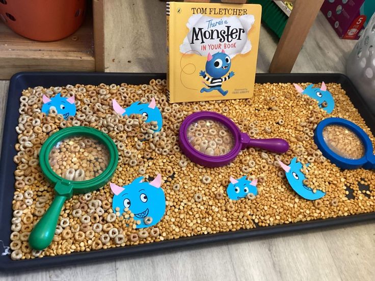 a tray filled with cereal and magnifying glasses next to a book about monsters