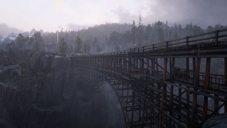 a bridge over a river surrounded by mountains and trees on a foggy day in the middle of winter