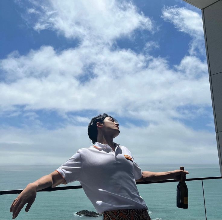 a man standing on top of a balcony next to the ocean with his arms outstretched