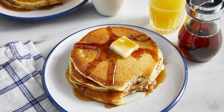 pancakes with butter and syrup on a plate next to glasses of orange juice, milk and honey