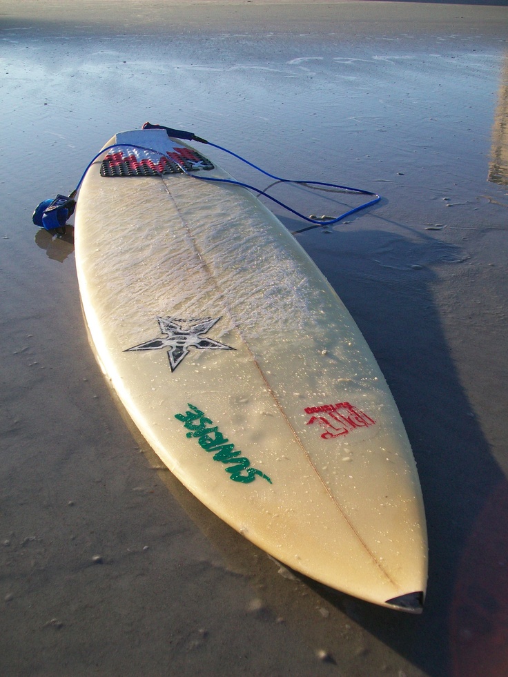 a surfboard is laying on the sand at the edge of the water, with writing on it