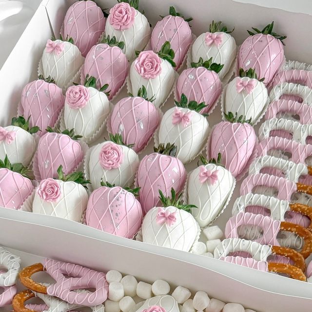 a box filled with lots of pink and white decorated strawberries next to pretzels