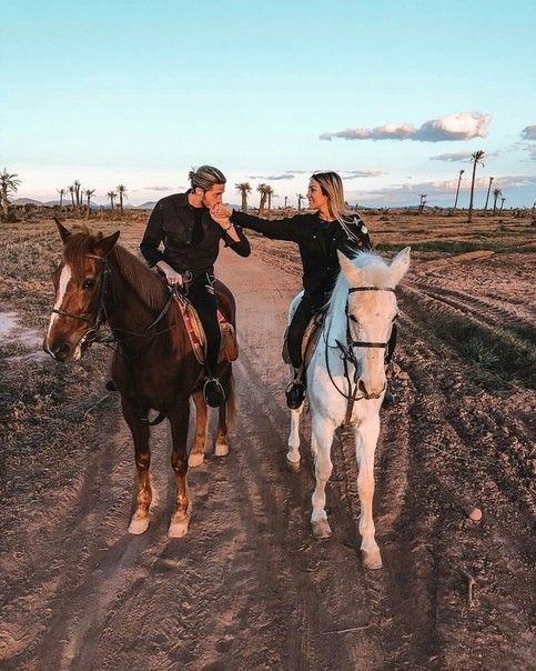 two people riding horses on a dirt road