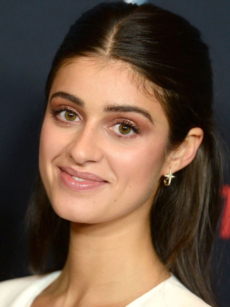 a close up of a person wearing a white dress and smiling at the camera with her hair in a pony tail