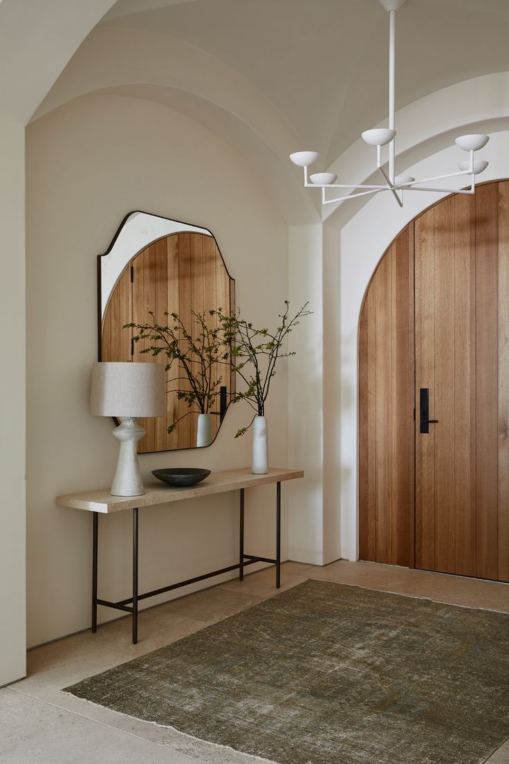 a room with a table, mirror and vases on the wall next to it