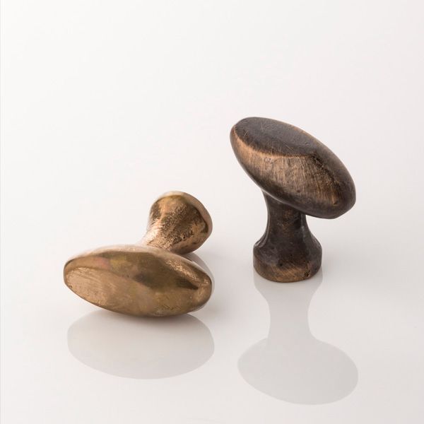 two bronze knobs on a white surface with reflections in the floor and one has an oval handle