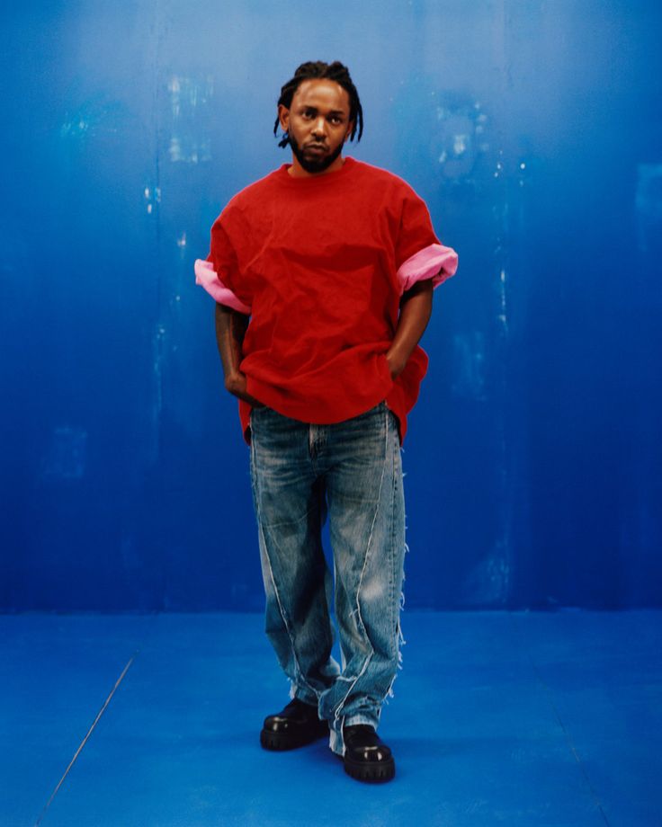 a man with dreadlocks standing in front of a blue background wearing a red shirt