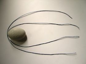 an object made out of wire with a rock on it's side and two needles sticking out of the middle