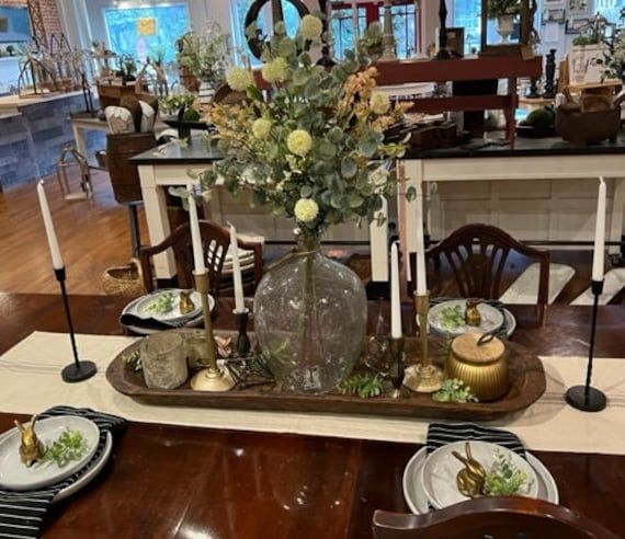 a dining room table set with plates and flowers on the centerpiece, along with other place settings