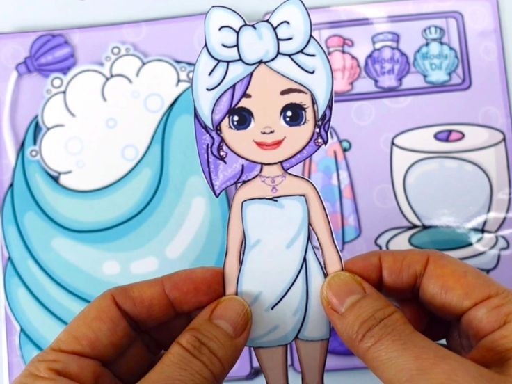 a person holding up a cut out of a doll in front of a bathroom scene