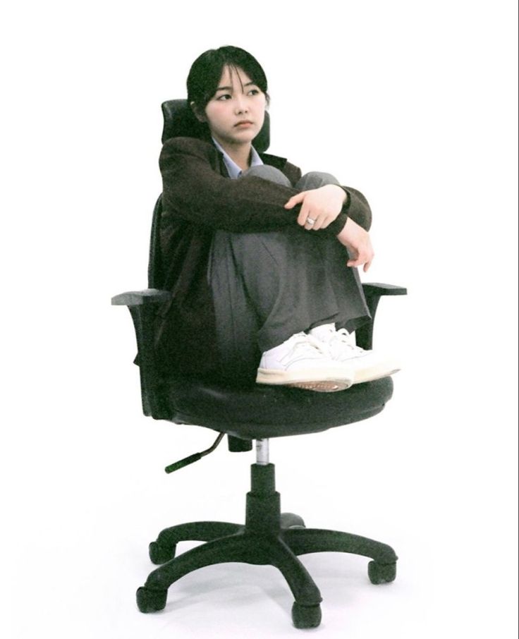 a woman sitting on top of an office chair with her arms folded over her head