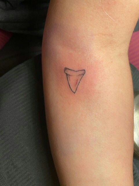 a small tattoo on the arm of a woman with a tooth shaped object in it