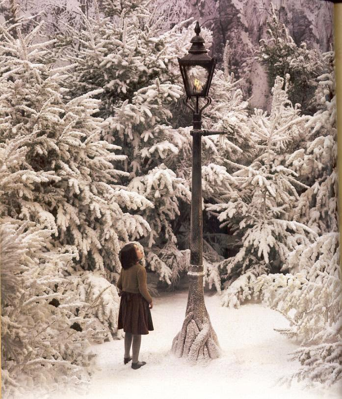 a woman standing in front of a street light surrounded by snow covered trees and evergreens