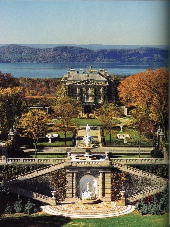 an aerial view of a large mansion in the middle of trees and water with mountains in the background