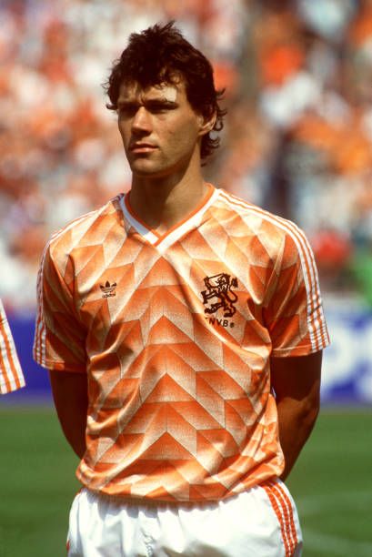 the soccer player is standing in front of an orange and white shirt with his hands on his hips