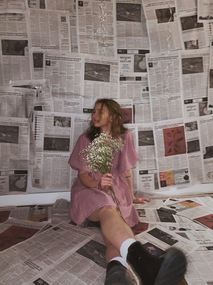 a woman sitting on the floor with flowers in her hand and newspapers all around her