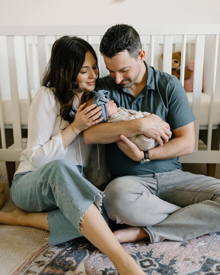 a man and woman sitting on the floor holding a baby