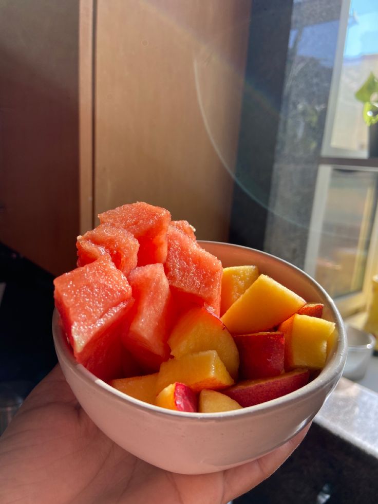 a person holding a bowl full of watermelon and apple slices in their hand