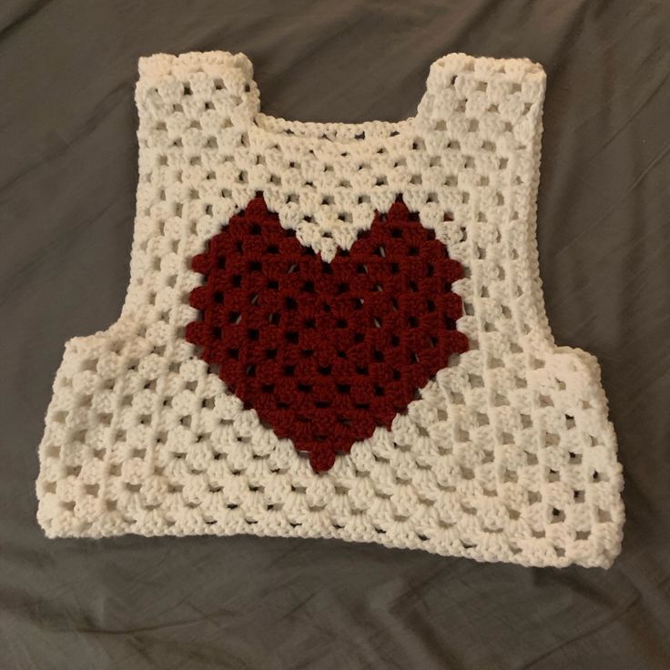 a crocheted white and red sweater with a heart on the front, sitting on a bed