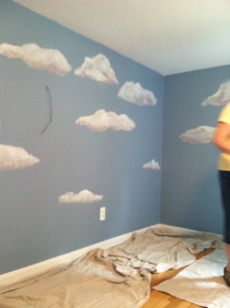 a woman standing on top of a wooden floor next to a wall with clouds painted on it