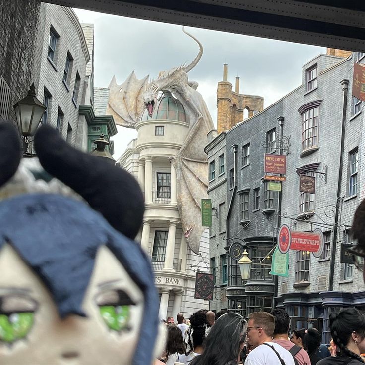 a crowd of people walking down a street next to tall buildings with dragon heads on them