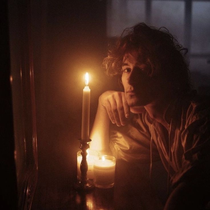 a man sitting in front of a candle with his hand on the table next to it