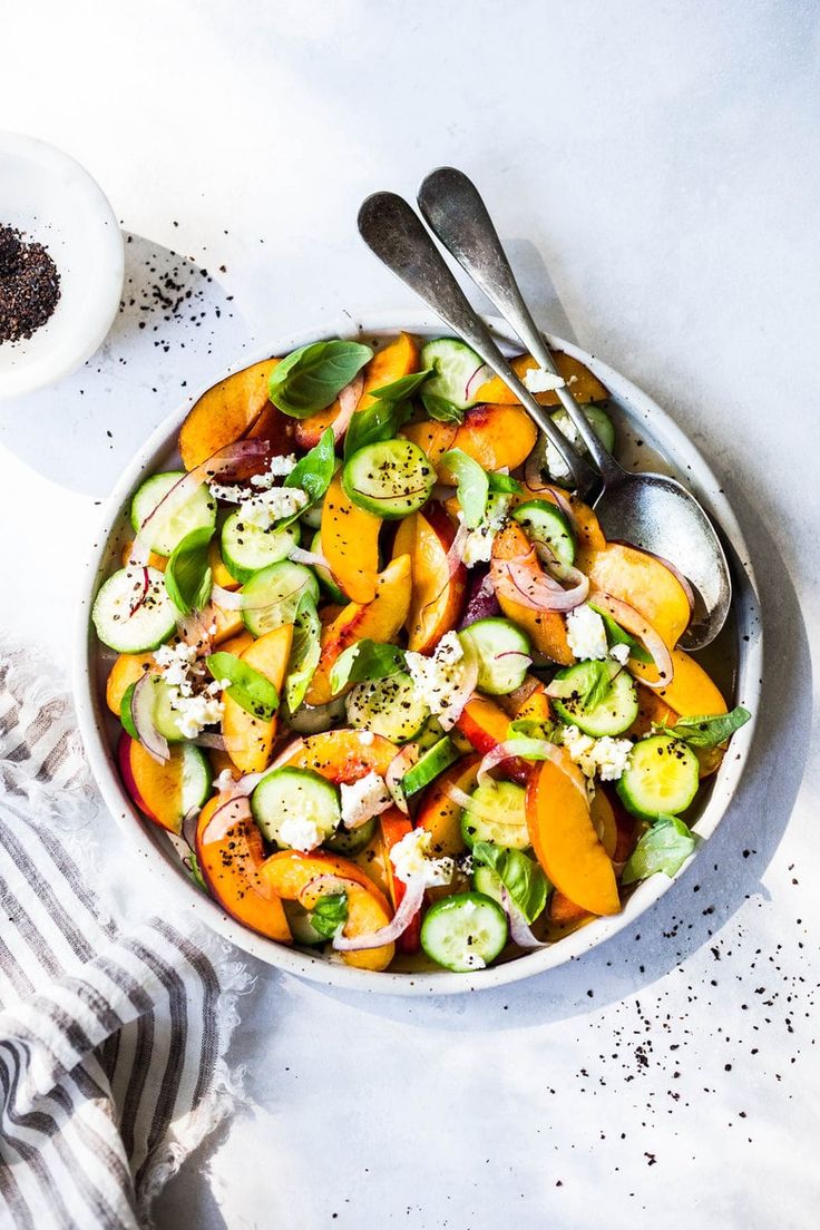 a white bowl filled with vegetables next to two spoons on top of a table