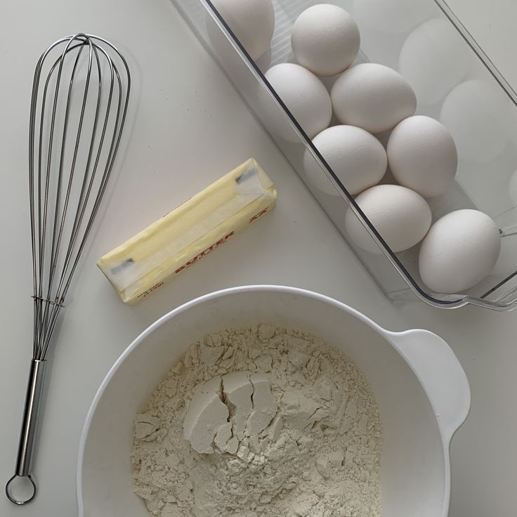 eggs, butter and flour in a bowl next to a whisk on a counter