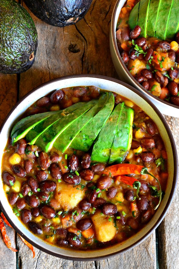 two bowls filled with beans and avocado on top of a wooden table