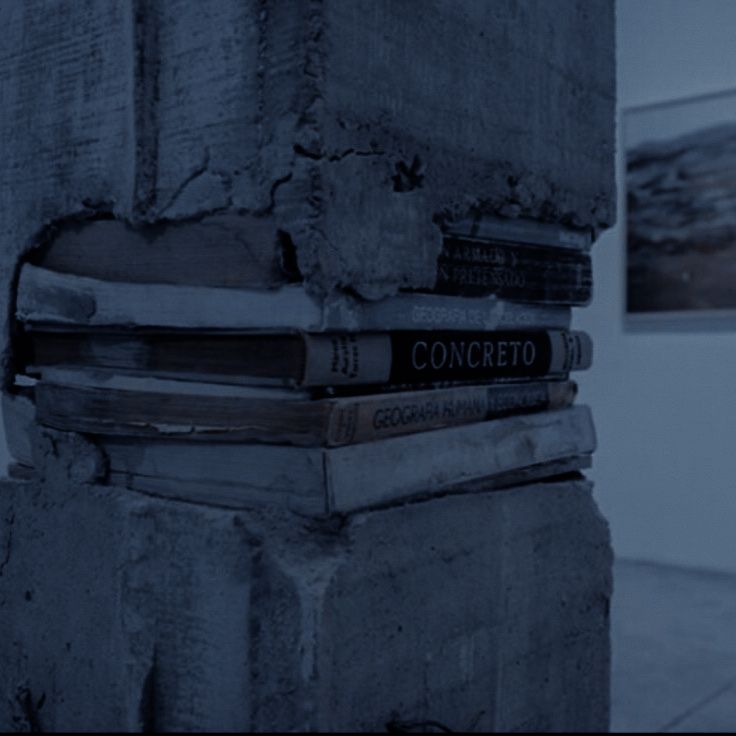 several books stacked on top of each other in front of a wall with two paintings