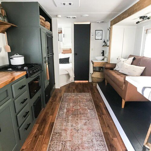 the interior of a tiny home with wood flooring and green cabinets, an area rug on the floor