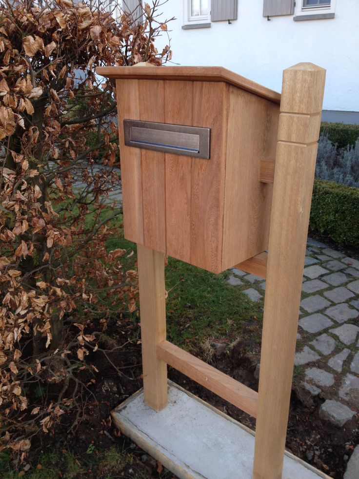 a wooden mailbox sitting on top of a cement slab next to a tree and bushes