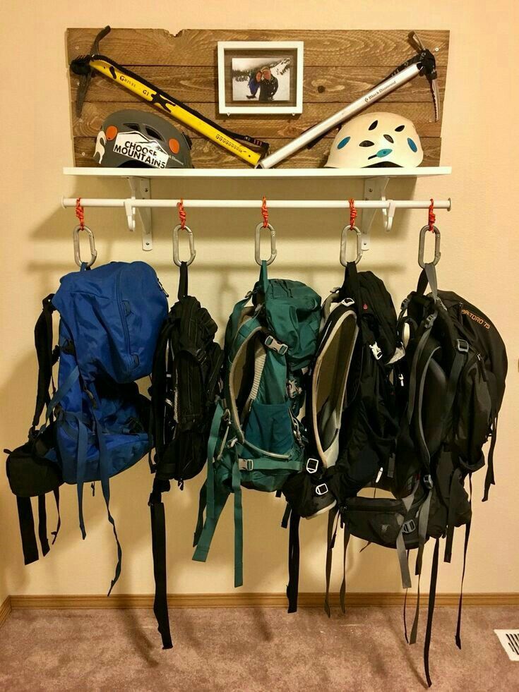 several backpacks and helmets are hanging on a wall with pegs to hold them