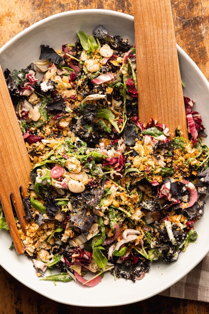 a white bowl filled with salad and two wooden spoons on top of the bowl