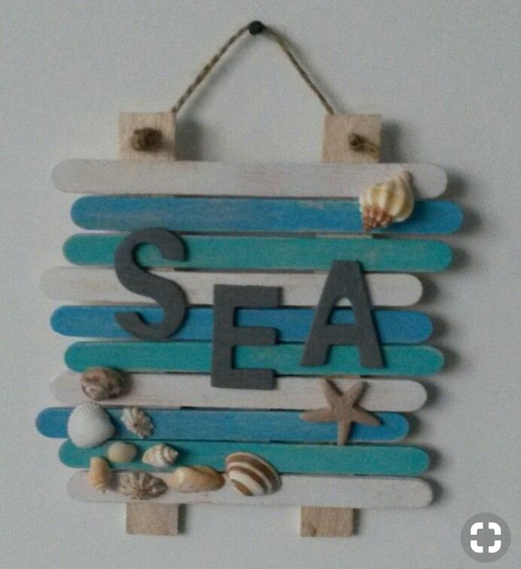 a wooden sign that says sea next to seashells and starfish on a white wall