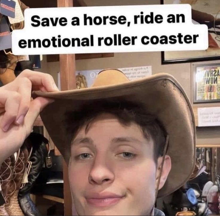 a young man wearing a cowboy hat and holding his hand up to the top of his hat