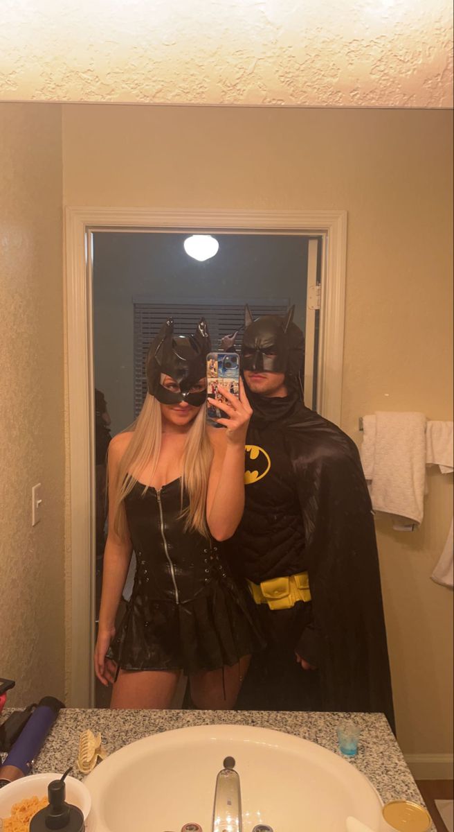 a woman in a batman costume taking a selfie with a man dressed as batman