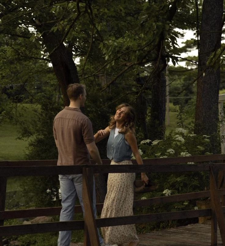 a man standing next to a woman on top of a wooden bridge in the woods