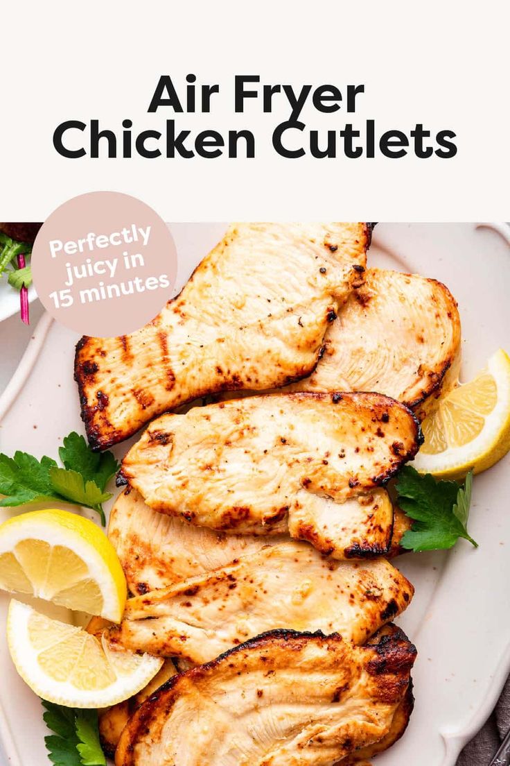 grilled chicken cutlets on a white plate with lemon wedges and parsley