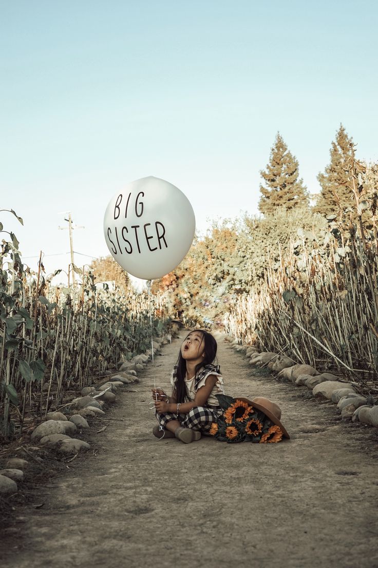 a woman sitting on the ground with a big sister balloon above her head