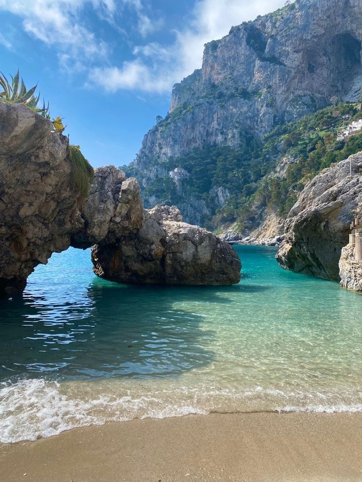 the water is crystal blue and there are rocks sticking out of the water in front of it